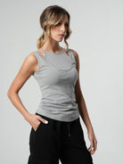 A woman wearing a sleeveless gray fitted top with spaghetti straps and a round neckline, paired with black pants.